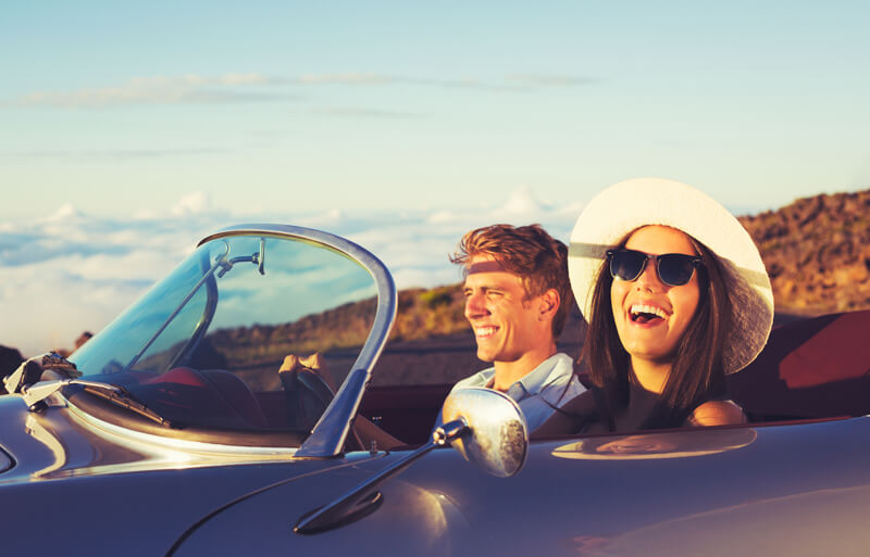 happy couple driving in convertible with the coast in the background